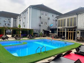 A swimming pool with lounge chairs and a building with multiple windows and air conditioning units. - LEADWORT HOTELS (Port Harcourt)