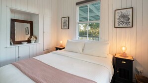 A bedroom with a large bed, two bedside tables with lamps, a window with a view, and framed artwork on the walls. - Lakeview Cottage in Mooloolah Valley: Pool & Sauna (Mooloolah Valley)