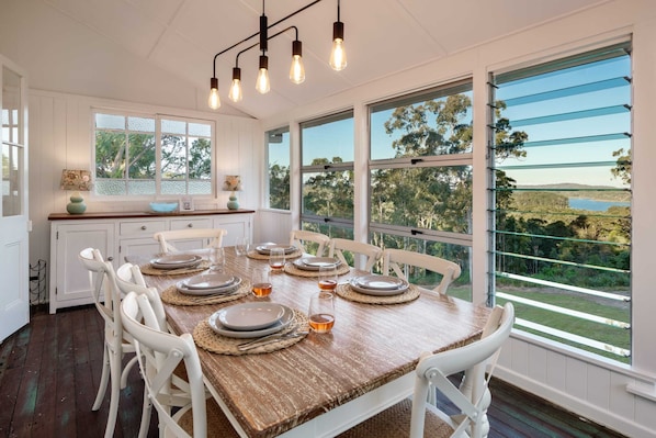 Enjoy meals with family and friends at this dining area, featuring a rustic table set for six and large windows offering a view of the outdoors.