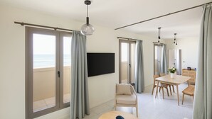 A modern living room with a large sliding glass door to the balcony, a flat-screen TV mounted on the wall, a round wooden coffee table, and a dining area with a wooden table and chairs. - Hôtel La Suite (Biarritz)