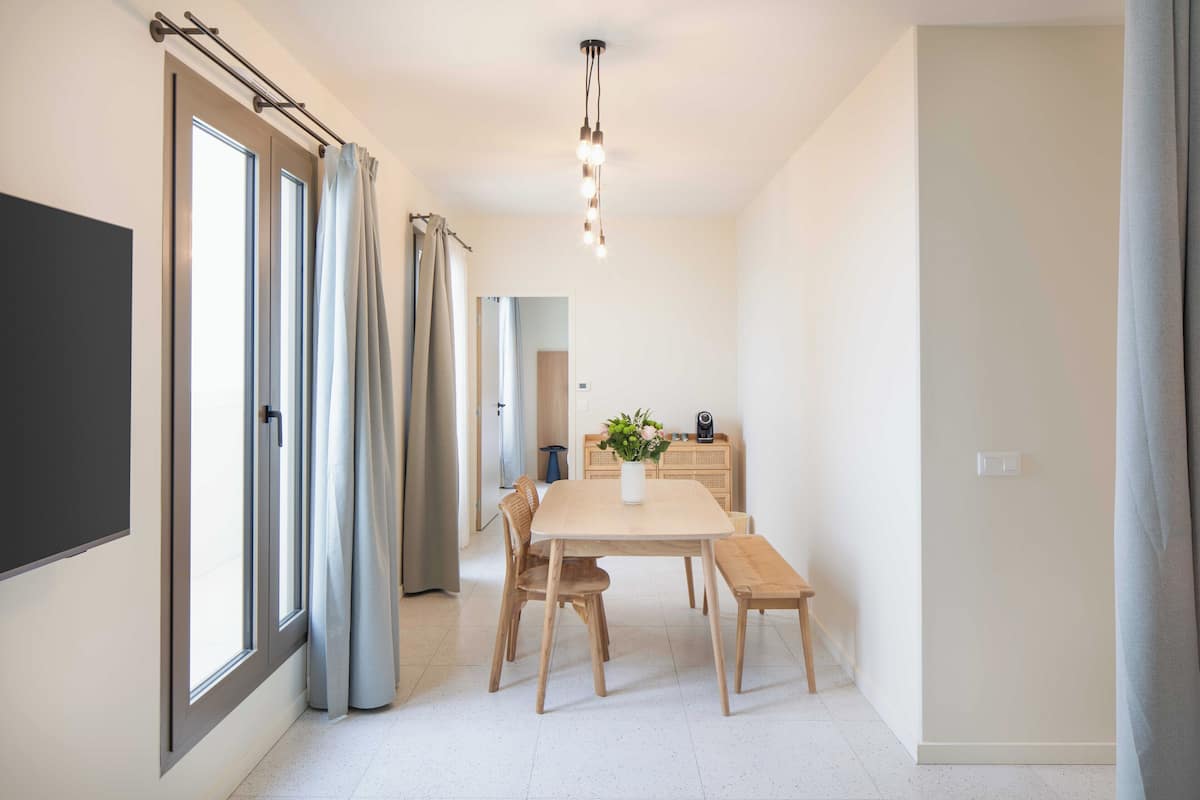 Un espace repas moderne avec une table en bois, des chaises et un banc. On peut voir un vase rempli de fleurs sur la table, et un luminaire suspendu au plafond.