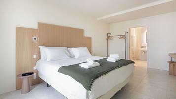 A modern hotel room with a large bed, a bedside table, a waste bin, and a bathroom visible through an open door.