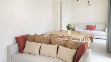 Una sala de estar moderna con un sofá, una mesa redonda de madera y una zona de comedor con mesa y sillas.