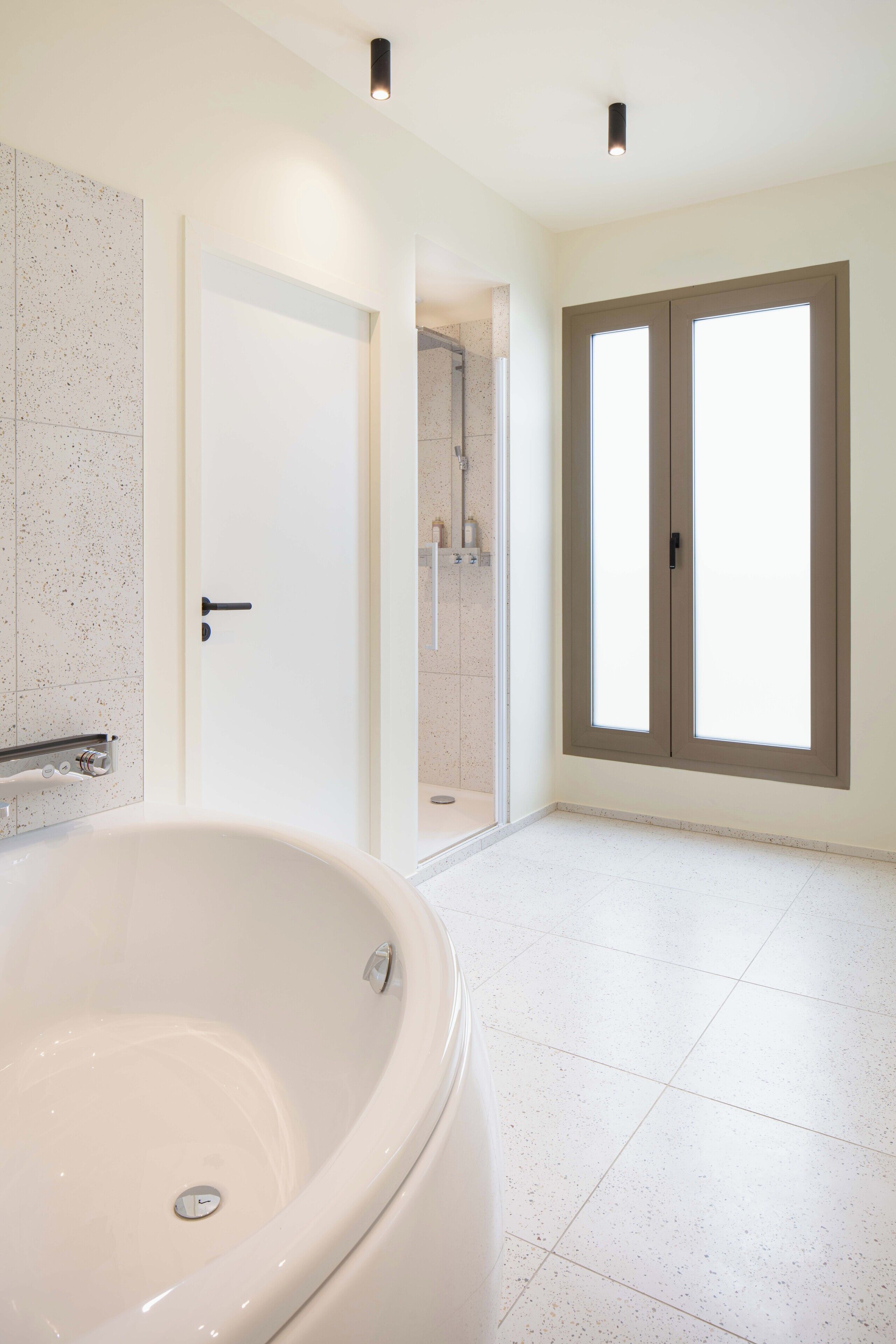 A modern bathroom with a freestanding bathtub, a shower area, and a large window with a view.