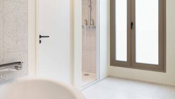 A modern bathroom with a freestanding bathtub, a shower area, and a large window with a view.