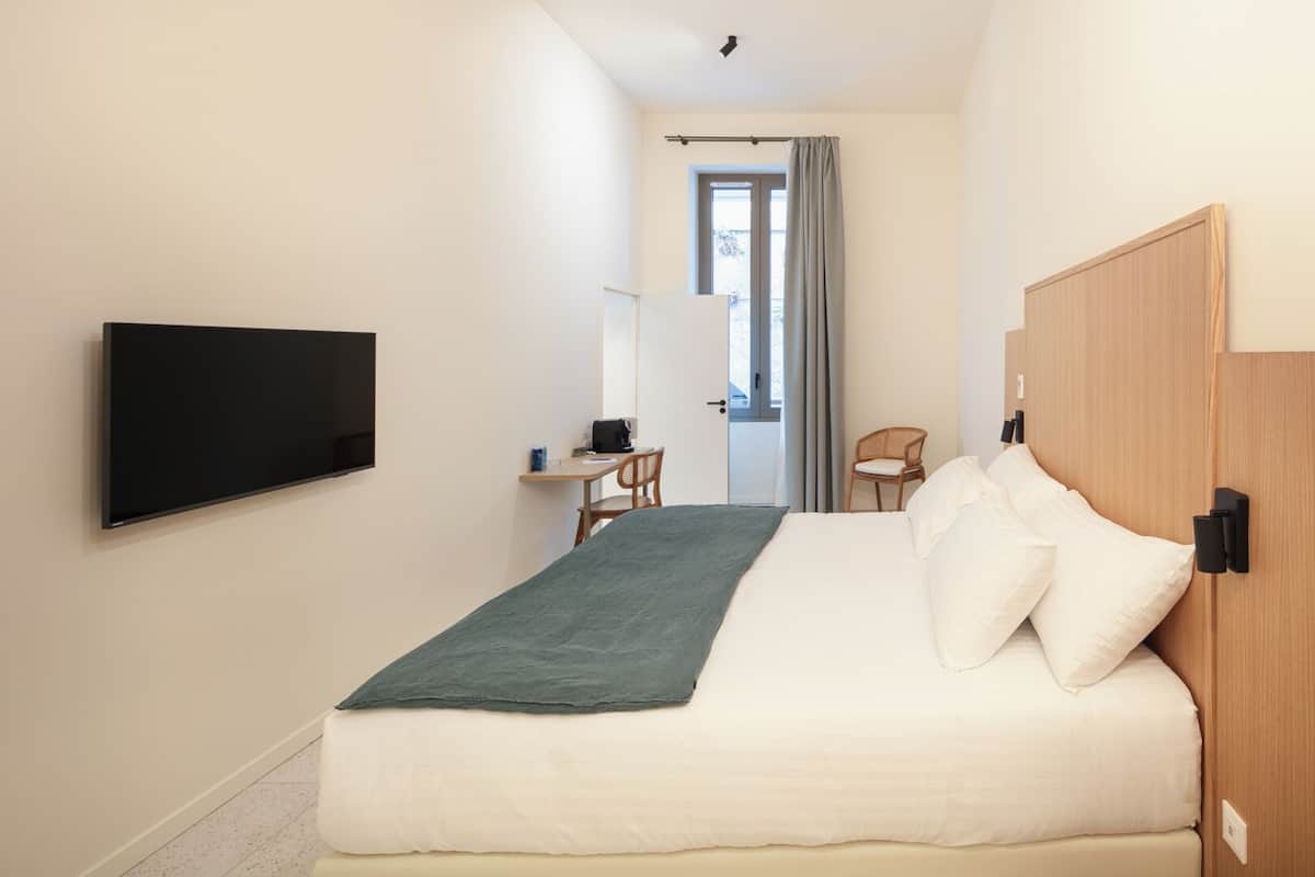 Une chambre à coucher comprenant un lit, un bureau, une chaise, un téléviseur et une fenêtre avec des rideaux.
