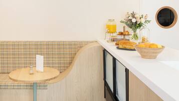 A modern kitchen with a wooden bench, a round table, and a breakfast setup including a fruit bowl and a vase with flowers.