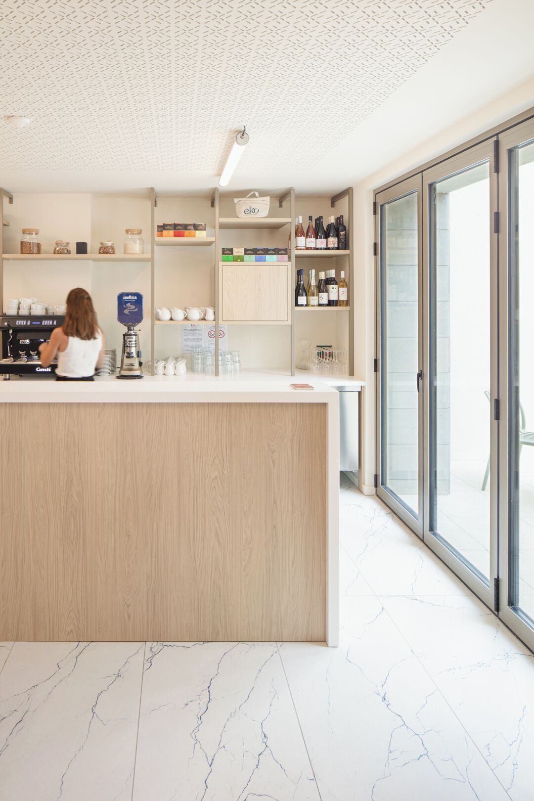 A modern bar area with a wooden counter, shelves with bottles, and a coffee machine.