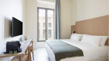 Une chambre d’hôtel avec un lit, un bureau avec un ordinateur, une télévision et une fenêtre avec des rideaux.