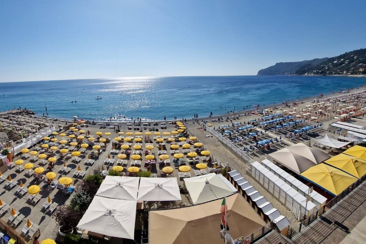 Un hotel frente a la playa con filas de tumbonas y sombrillas, una piscina y vistas al mar.