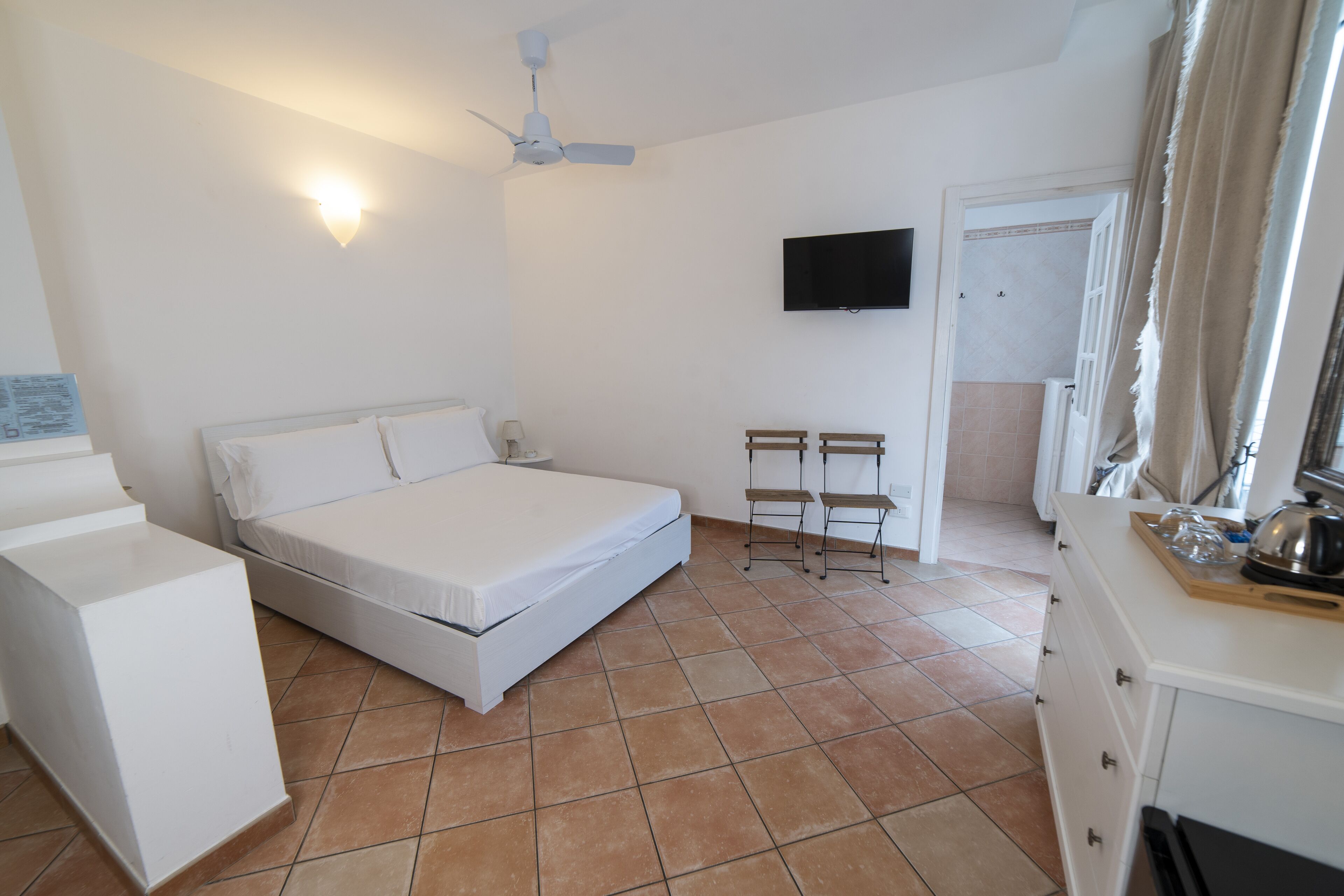 A bedroom with a bed, a desk, a chair, a television, and a bathroom door.