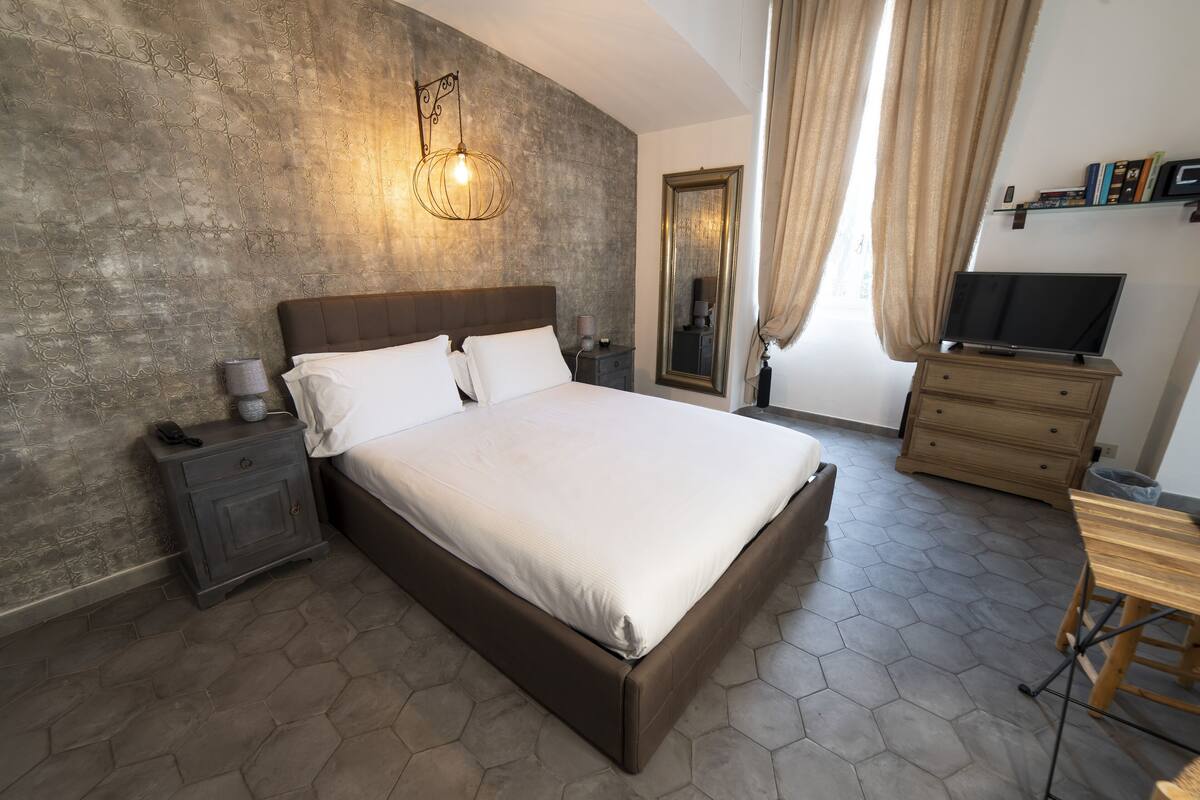 Un dormitorio moderno con una cama grande, una mesita de noche, un aparador, un televisor y un espejo.