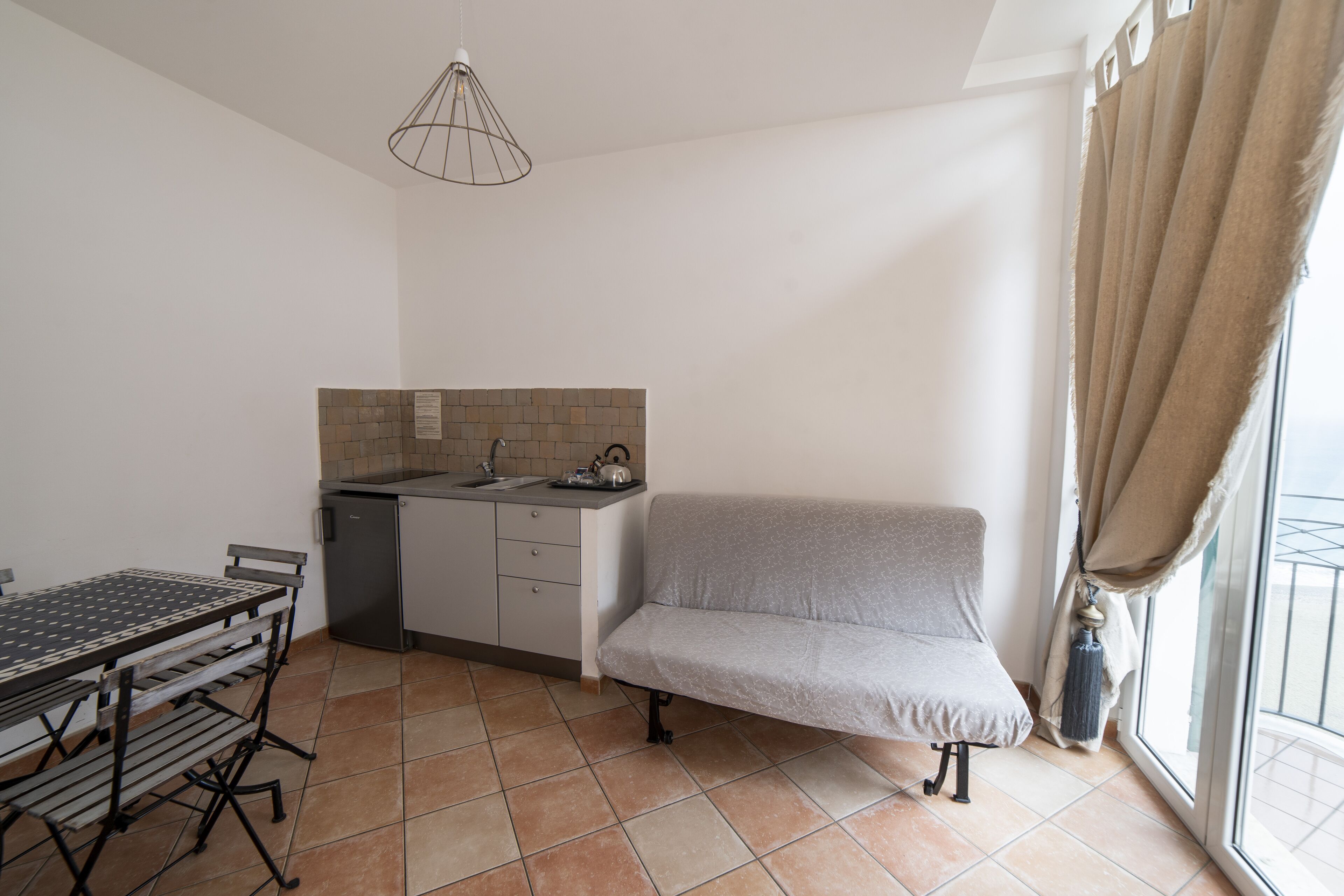 A compact kitchen with a dining table, a sofa, and a window with curtains.