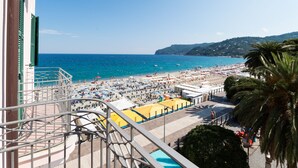 A balcony with a view of a beach, a pool, and a building with green shutters. - Hotel Miramare - Spotorno (Spotorno)