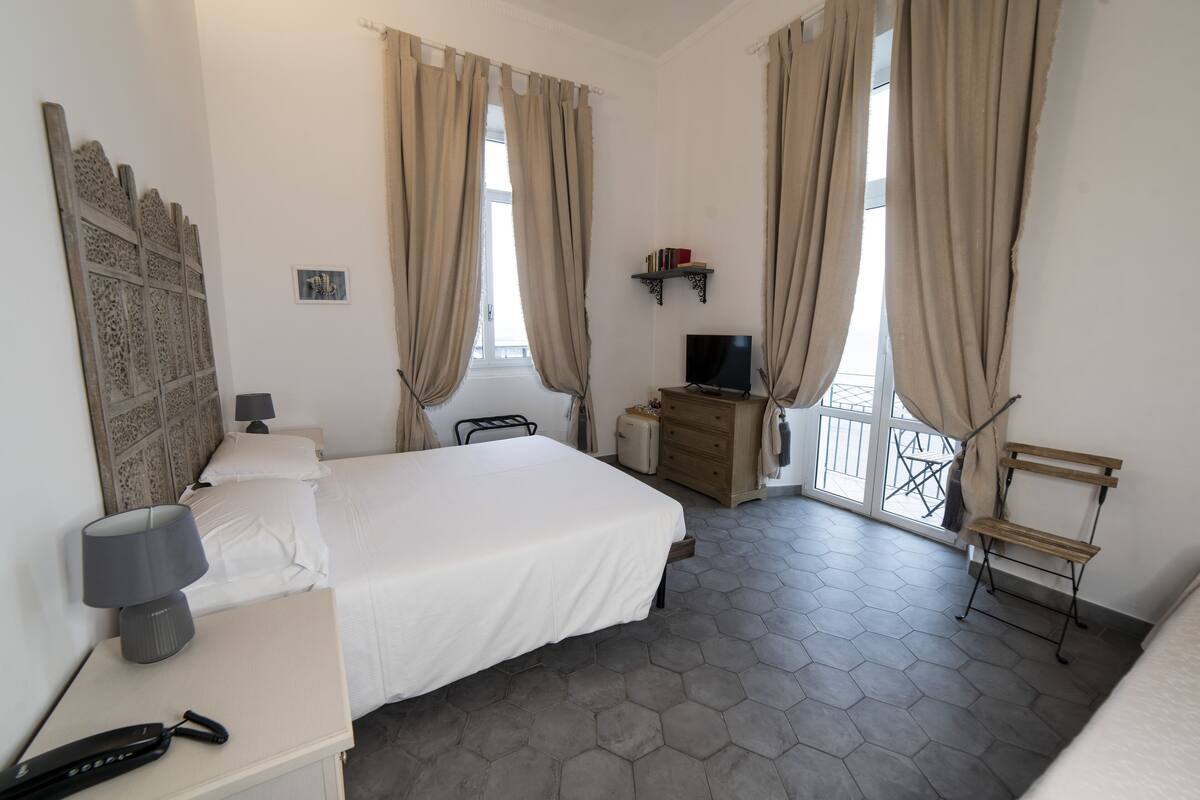 Habitación de hotel con cama, escritorio con lámpara, televisión, cómoda de madera y una silla.