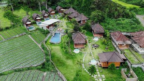An aerial view of a resort with multiple bungalow-style accommodations, a central swimming pool, and surrounding lush greenery. - Cabana Bali Villa (Kintamani)