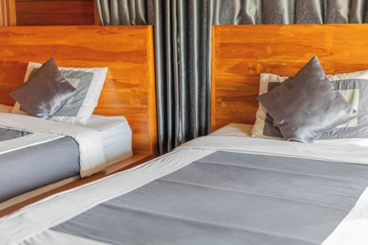 Habitación de hotel con dos camas, cada una con cabecero de madera, ropa de cama gris y una almohada.