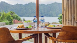 A wooden table with plates of food, two water bottles, and a bowl of salad. - Cabana Bali Villa (Kintamani)
