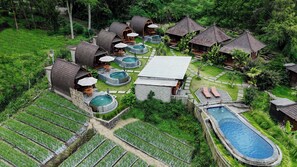Vista aérea de un resort con varias cabañas, una piscina central y exuberante vegetación circundante.