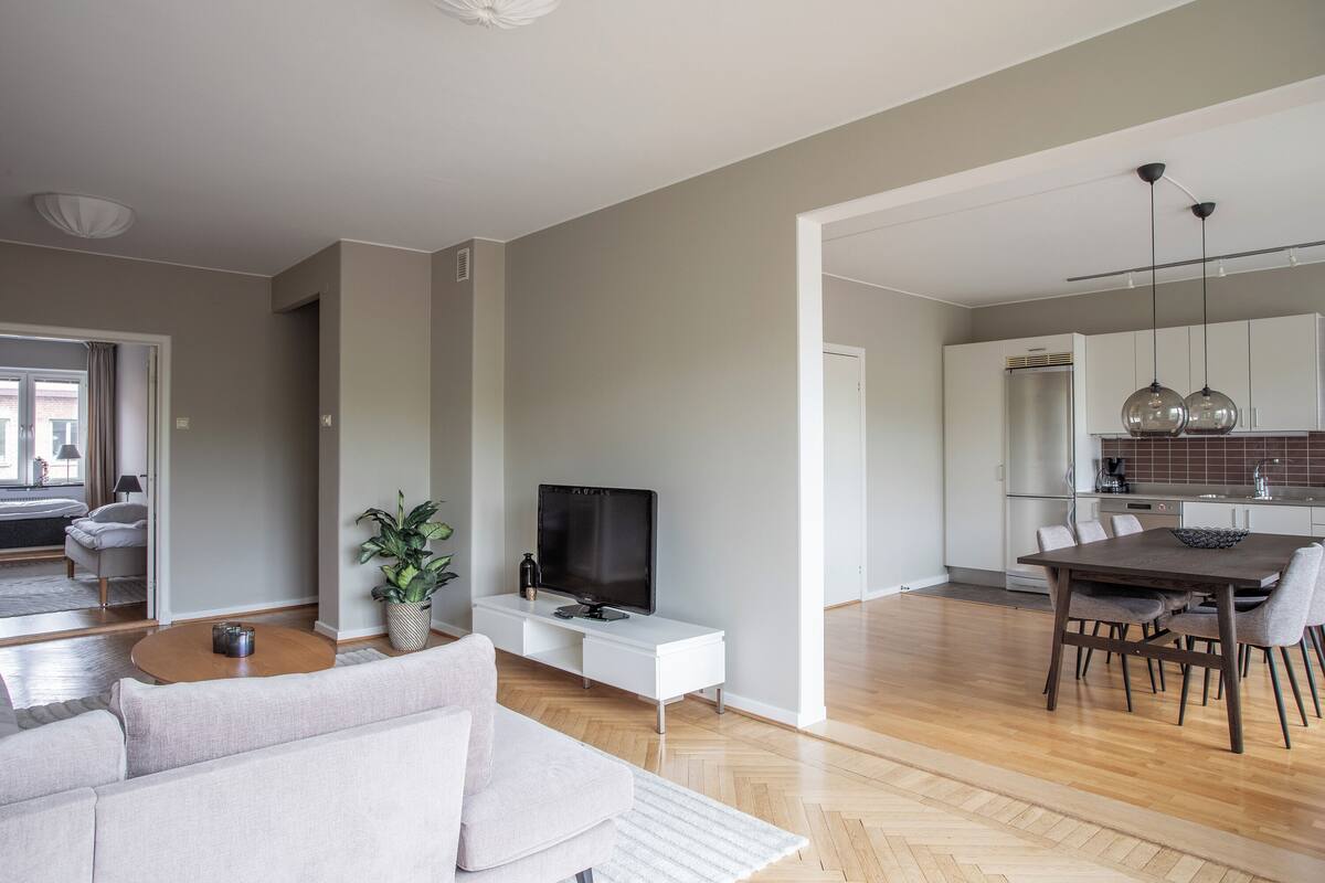 A modern living room with a sofa, a coffee table, a TV, and a dining area with a table and chairs.