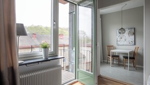 A modern room with a sliding glass door leading to a balcony, a white radiator, a small table with two chairs, and a potted plant on the windowsill.