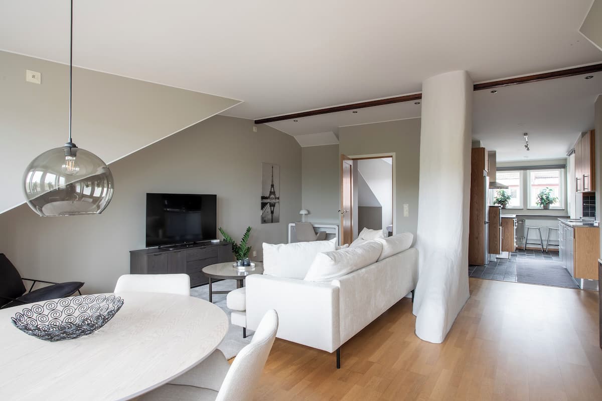 A modern living room with a white sofa, a dining table with a patterned bowl, and a TV.