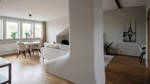 A spacious living area with a high ceiling, a dining table with chairs, a sofa, and a large window with a view of greenery. - HeyStay Lagerbring (Gothenburg)
