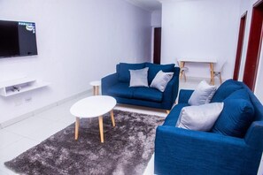 A modern living room with a blue sofa, a white coffee table, and a flat-screen TV mounted on the wall. - Shortlet Homes Port Harcourt (Port Harcourt)