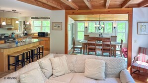 A cozy kitchen with wooden beams, a dining area with a chandelier, and a living room with a large sofa.