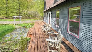 A wooden deck with a pergola, a bench, and a house with a red window frame.