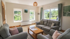 Ein Wohnzimmer mit einer Sofagarnitur, einem Couchtisch und großen Fenstern mit Blick auf Grünflächen.