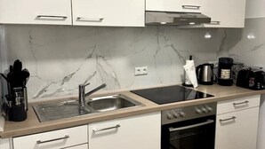Une cuisine moderne avec des meubles blancs, une cuisinière noire, un évier et un pare-feu en marbre.