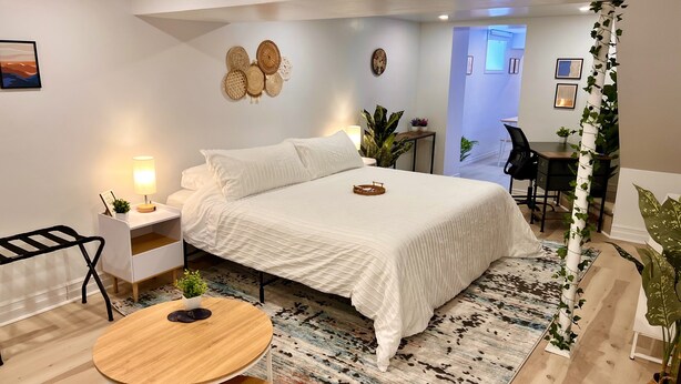 A modern bedroom with a large bed, bedside tables with lamps, a round wooden table, and a patterned rug. - The Boho Oasis: Spacious Deluxe Apartment, Close to All Amenities, Safe & Quiet (Windsor)