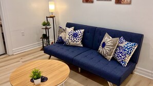 A modern living room with a blue sofa, decorative pillows, a wooden coffee table, and wall art. - The Boho Oasis: Spacious Deluxe Apartment, Close to All Amenities, Safe & Quiet (Windsor)