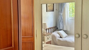 A bedroom with a wooden door, a bed with a white comforter, a nightstand with a lamp, and a window with curtains. - Casa Primera Línea en Berria - Chalet Pitu 17801 (Berria)