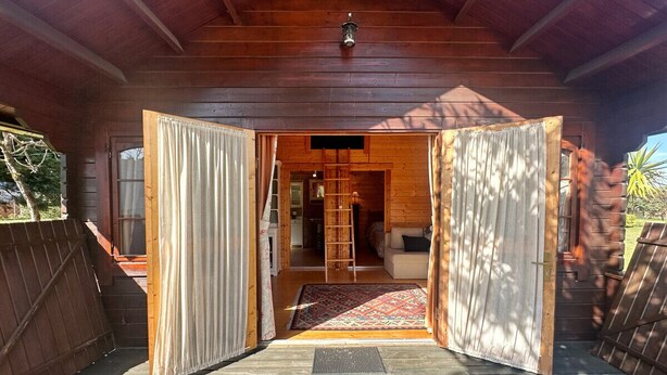 A wooden cabin with an open door leading to a living area with a couch and a ladder. - Casa Primera Línea en Berria - Chalet Pitu 17801 (Berria)