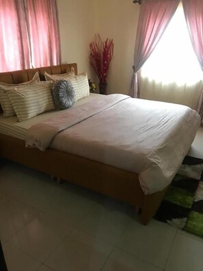 A bed with a wooden frame, a white bedspread, and striped pillows. - D Dov Guest House (Port Harcourt)