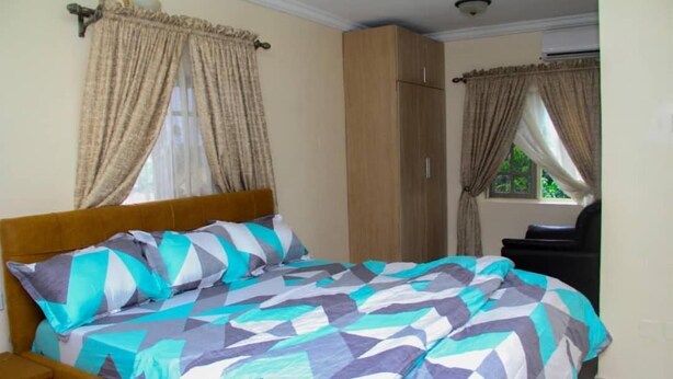 A bedroom with a bed, curtains, a wardrobe, and a window. - D Dov Guest House (Port Harcourt)