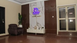 A lobby with a marble wall, a reception desk, a brown armchair, and a glass door. - D Dov Guest House (Port Harcourt)