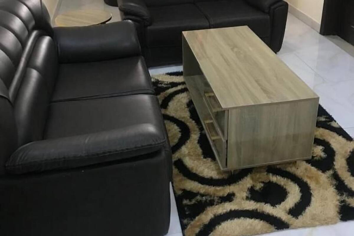 A living room with a black leather sectional sofa, a wooden coffee table, and a patterned rug.