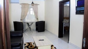 A compact living space with a sofa, a small table, a TV mounted on the wall, and a door leading to another room. - D Dov Guest House (Port Harcourt)