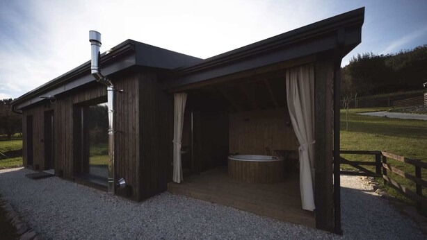 A modern wooden cabin with a glass door entrance, a hot tub, and a covered outdoor seating area. - CABAÑAS O RECUNCHO DO SOR. SETENTRIÓN (San Fiz)