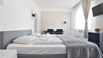 A modern hotel room with a large bed, a desk, two chairs, a flat-screen TV, and a window with curtains.