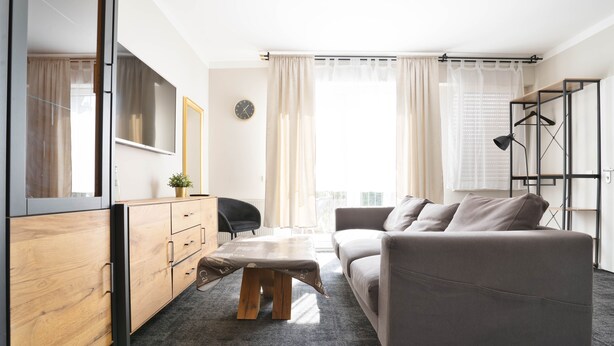 A modern living room with a grey sofa, wooden cabinet, and a small table. - Stilvolle Apartments in Bonn I home2share (Bonn)