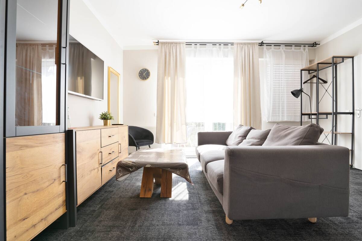 Een moderne woonkamer met een grijze bank, een houten kast en een kleine tafel.