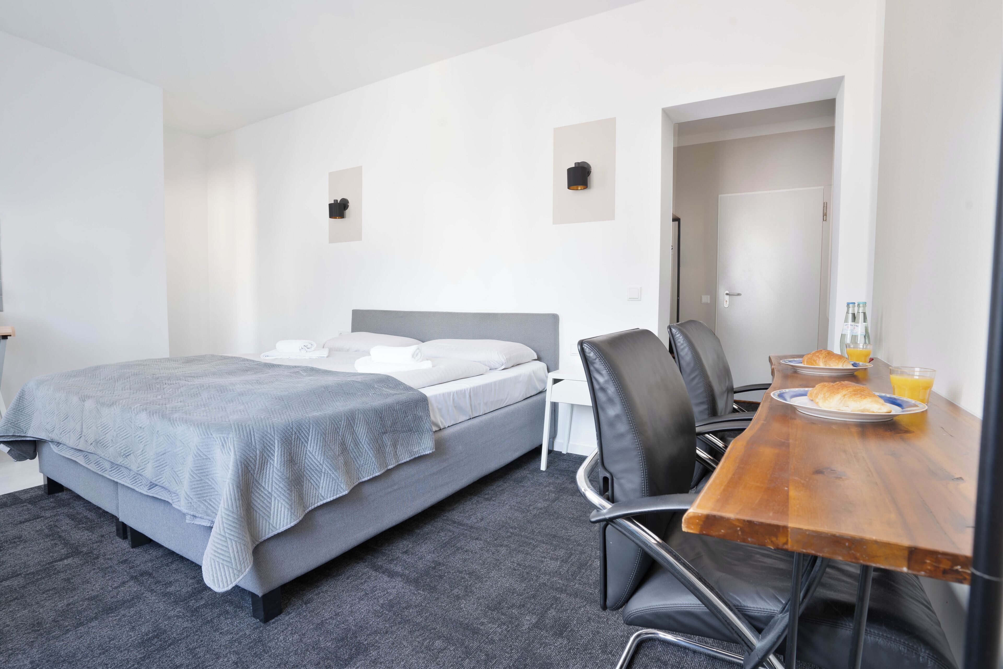 Habitación de hotel con cama, escritorio y sillas, y alimentos para el desayuno sobre la mesa.