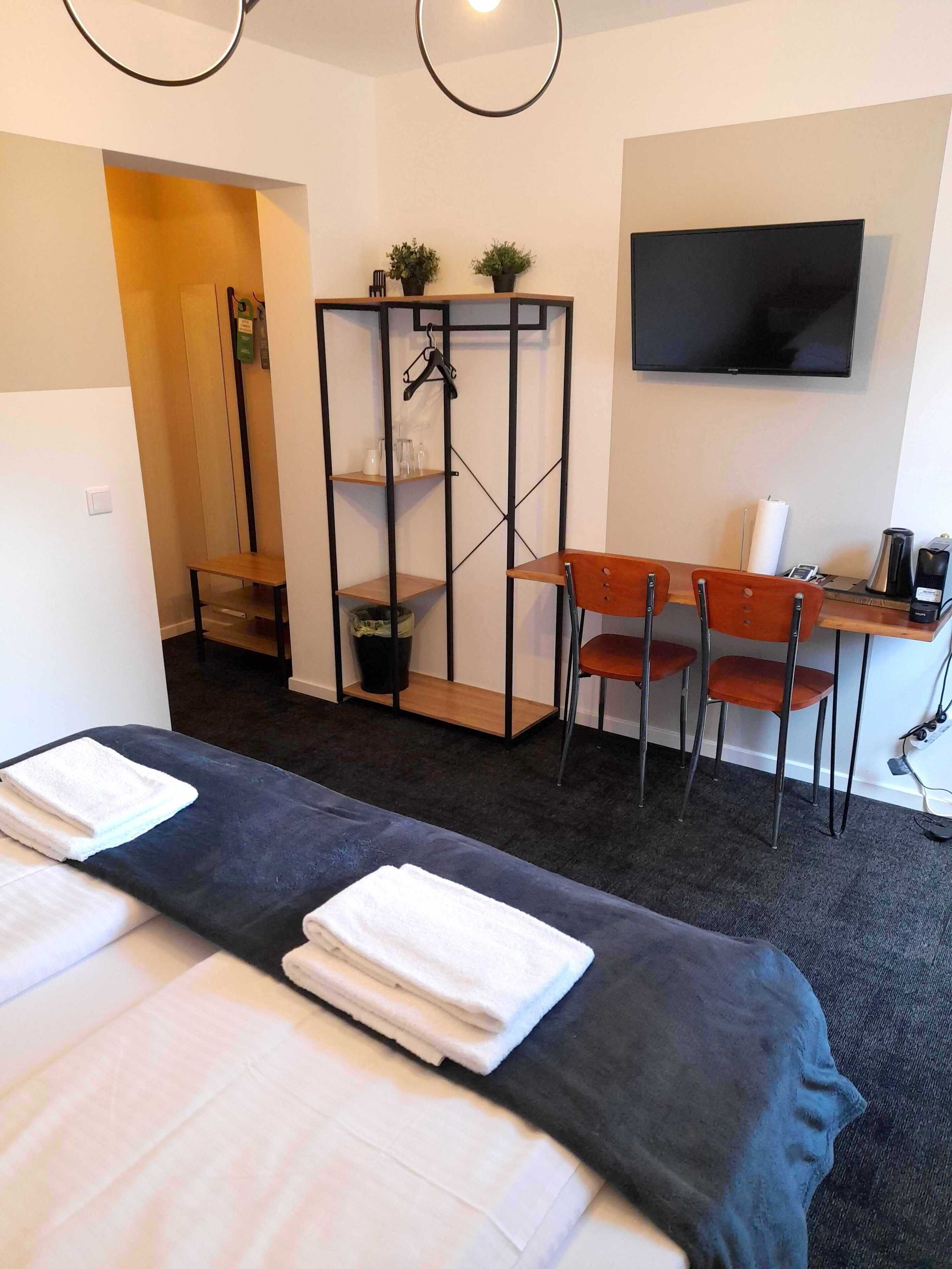 A hotel room with two beds, a desk, a chair, a TV, and a shelf with plants.