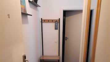 Un corridoio stretto con una panca di legno, una porta con un numero e uno specchio sulla destra.