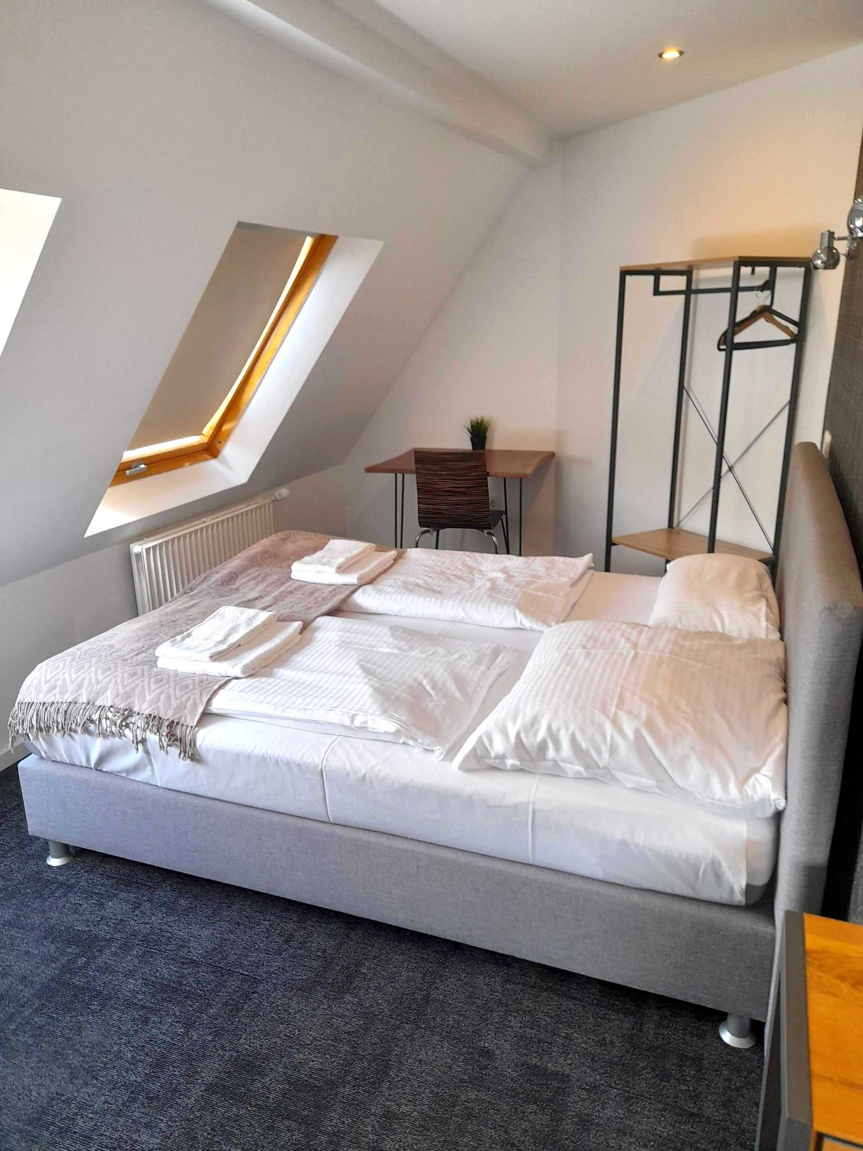 Une chambre moderne avec un grand lit, une lucarne, une petite table et un porte-vêtements suspendu.