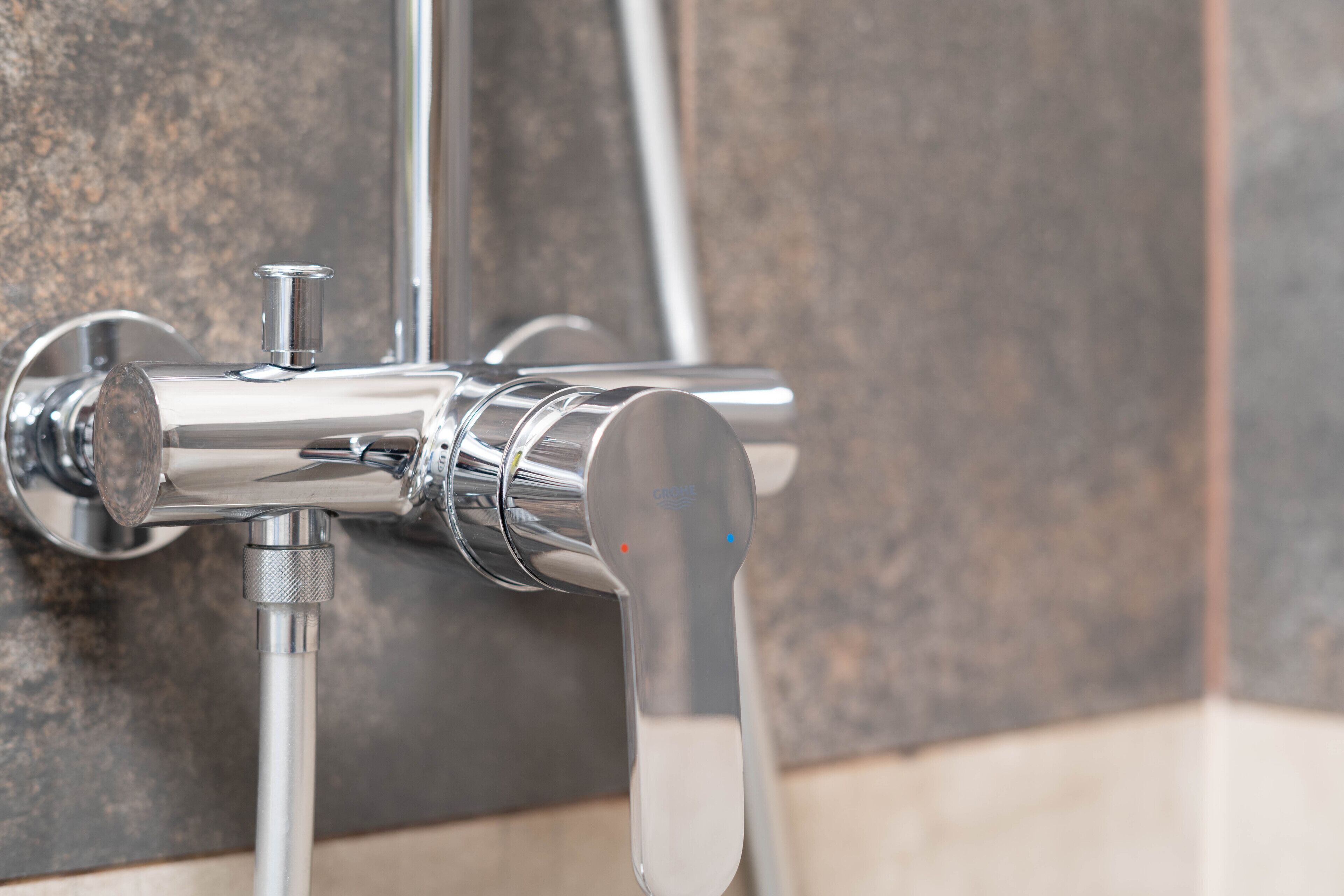 A chrome faucet with a single handle and a spout, mounted on a tiled wall.